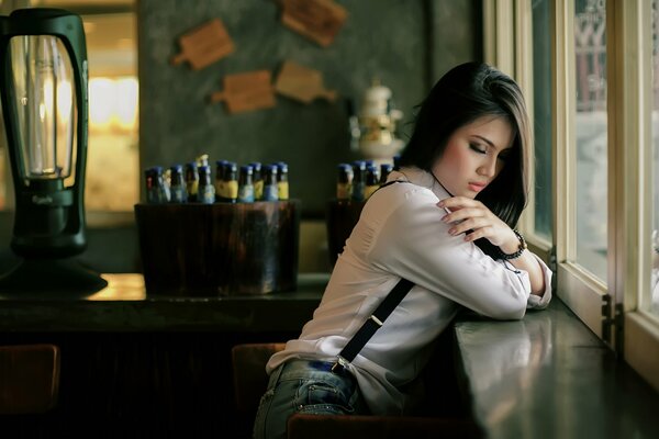 Una chica con camisa cerca de la ventana. Detrás de la botella