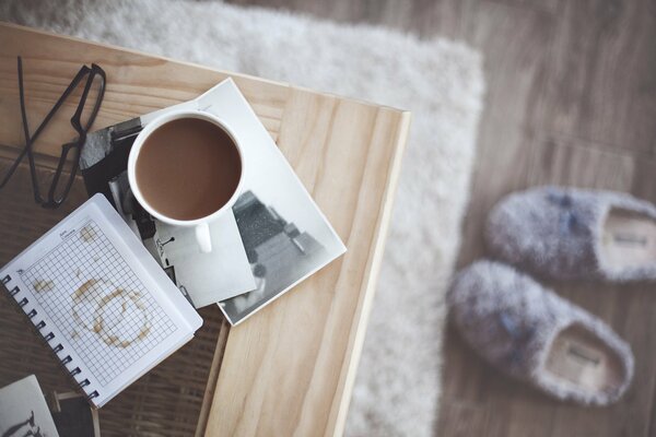 Una tazza di caffè sul tavolo accanto al quale ci sono comode pantofole