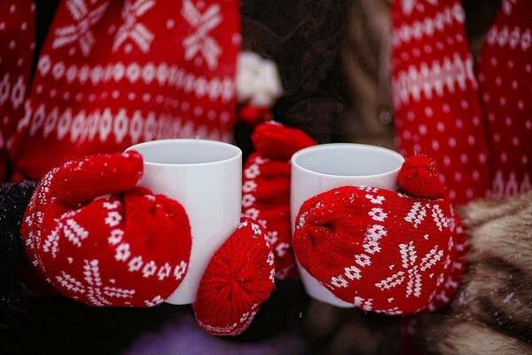 Las manos en los guantes rojos sostienen el vaso con el té