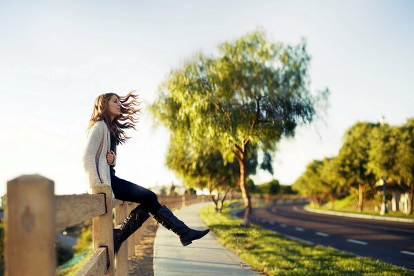 A girl on the street is sitting on a fence