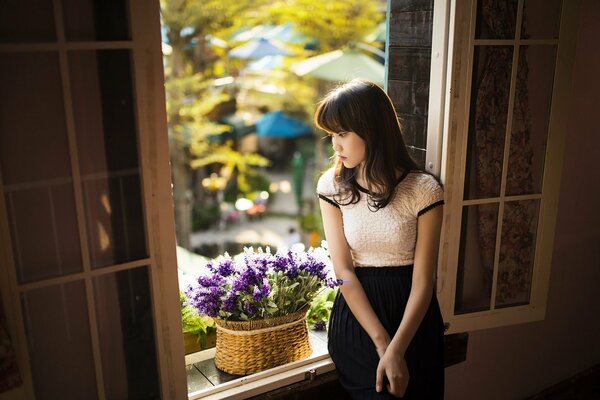 Chica asiática en la ventana con flores de color púrpura