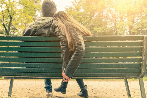 Una pareja se sienta en un banco verde y se toma de la mano