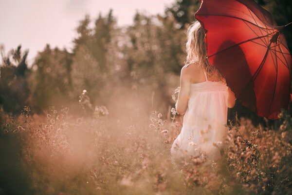 A girl with a red umbrella in a white dress against a forest background