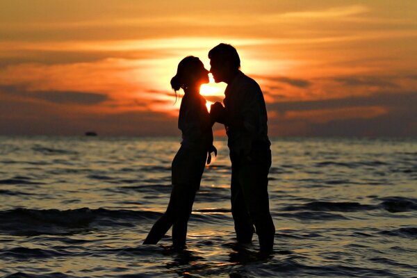 Two lovers in the sea on the background of sunset