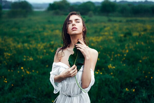Chica con una hoja de pie bajo la lluvia