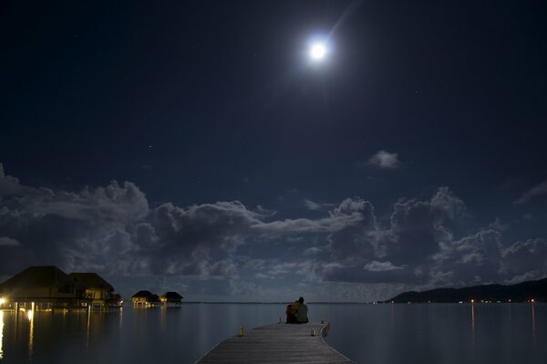 Dos en la orilla del mar mirando a la Luna