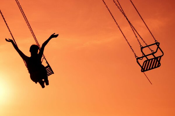 La fille sur l attraction avec les bras levés, sur fond de coucher de soleil