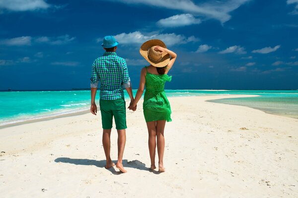 En los trópicos, una pareja pasea por la playa entre palmeras