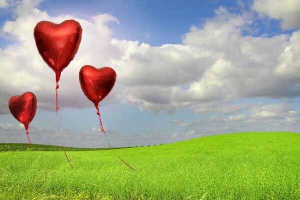 Red balloons in the form of hearts between the grass and the sky