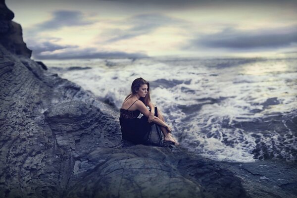 Sad girl sitting on a rock by the sea