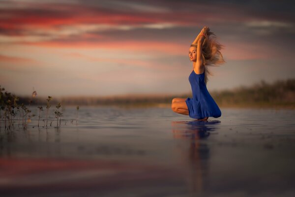 A girl in a blue dress at sunset on the shore of a lake