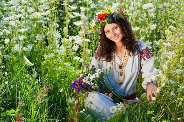 A girl with a wreath on her head is sitting in the grass