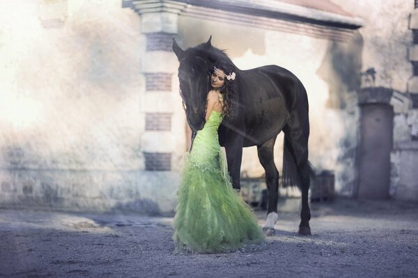 A brunette girl in a lush green dress with a flower in her hair hugs a horse