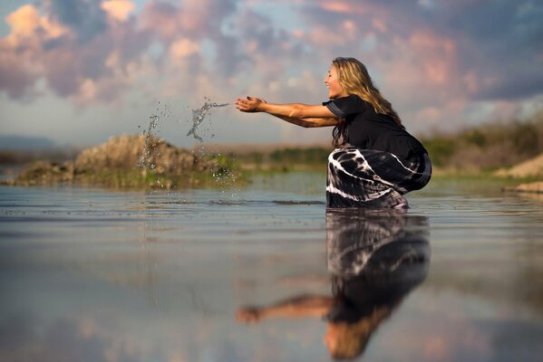 Happy girl on the shore of the lake with splashes of water