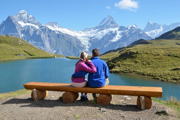 A couple sits on a bench and looks at the mountains