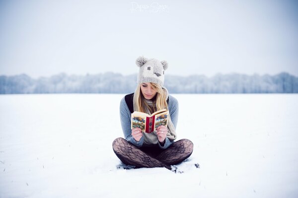 Fille dans un chapeau lit un livre sur la neige