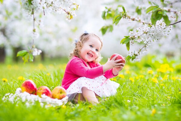 A joyful child with an apple in his hands is sitting on the grass