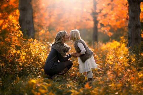 Daughter and mother kiss on the background of yellow trees