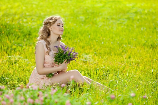 A blonde with a bouquet of wildflowers is sitting in a clearing