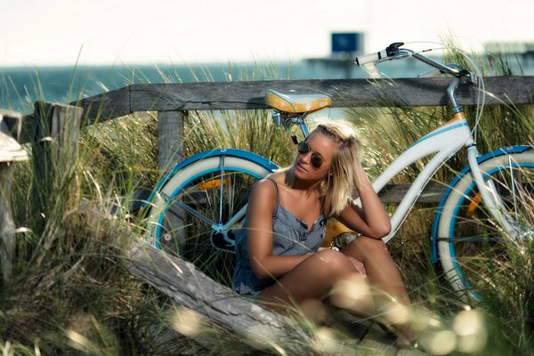 A girl is sitting by a bicycle in a meadow