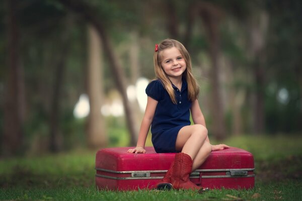 Fille assise sur une valise rouge