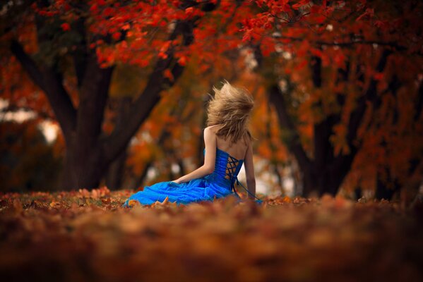 Mädchen im Kleid sitzt im Herbstwald