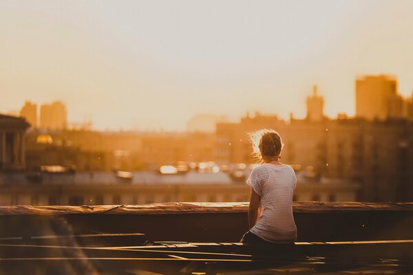 The girl is sitting alone on the roof and meets the dawn