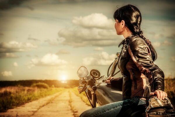 A girl with a motorcycle near the road at sunset