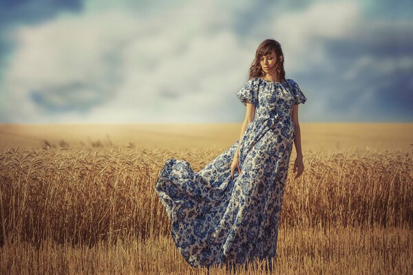 A girl in a fluttering dress stands in a field