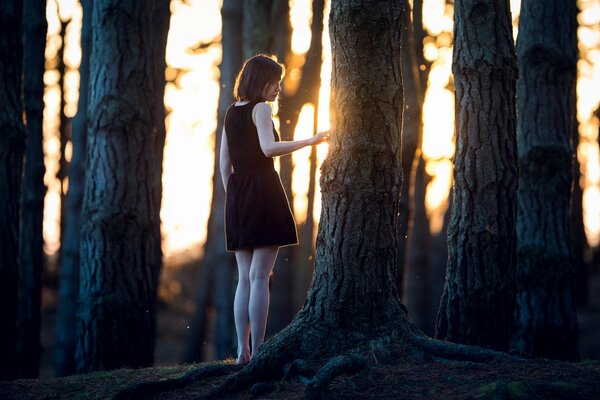 Chica con vestido negro cerca de un árbol