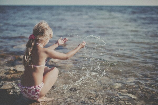 La niña en la orilla del mar se regocija en el verano, el sol