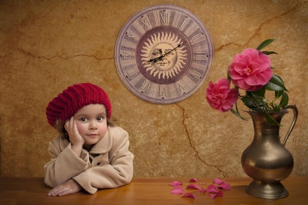 A little girl in a pink beret is sitting at a table with peonies