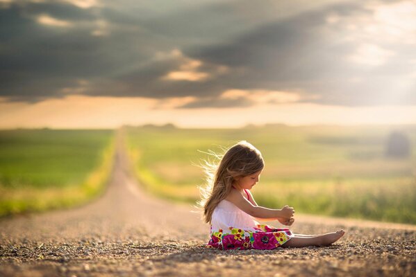 A little girl in a beautiful dress is sitting on the road