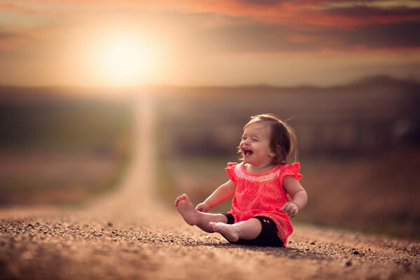 A cheerful little girl is sitting on the road