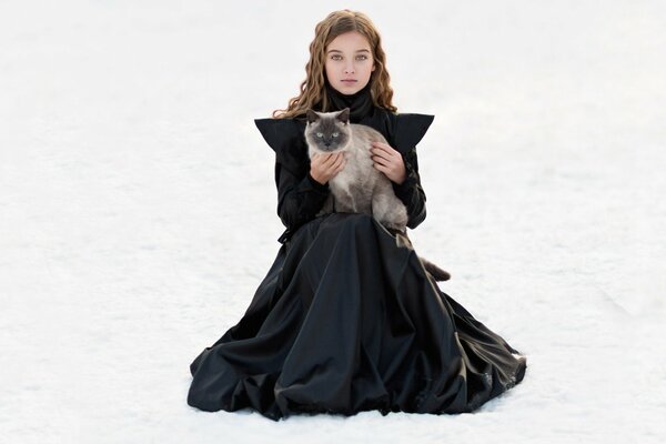 Foto de una niña en la nieve con un gato blanco