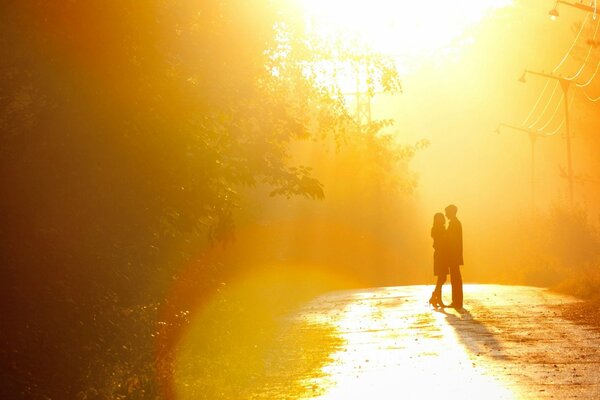 The couple is standing on the road in the rays of the sunset sun