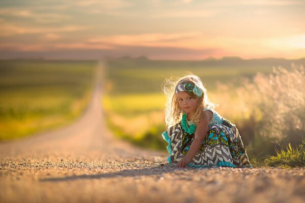 Bambina in vestito seduta sulla strada