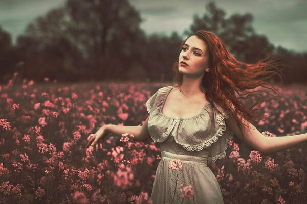 A red-haired girl with shikarny curls in a field with flowers