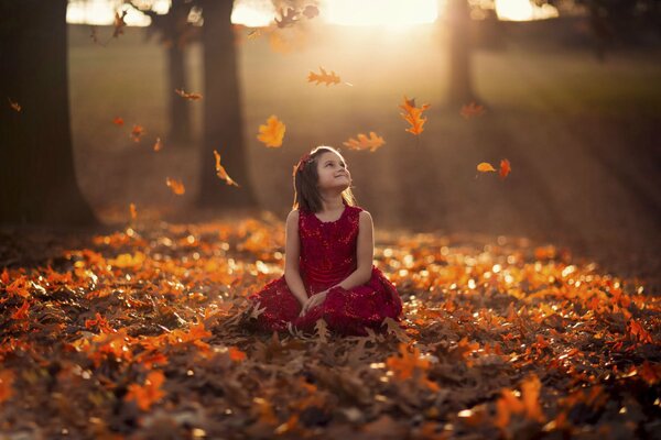 A girl sitting on orange leaves rejoices in autumn