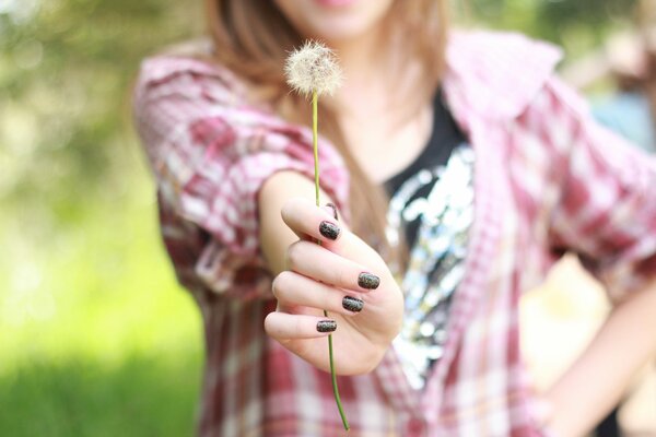 A girl s hand with a dandelion on a blurry background of nature