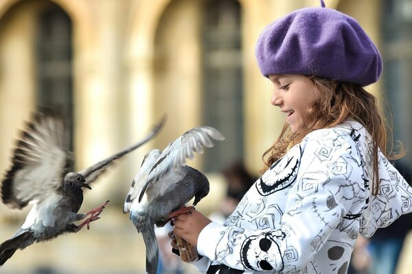 A girl in a hat feeds pigeons