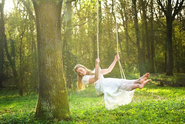 A girl in a white dress on a swing in the woods