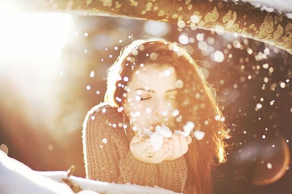 Hermosa chica soplando en los copos de nieve en sus Palmas