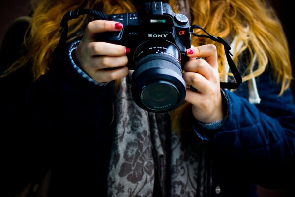 La ragazza con i capelli rossi e lo smalto rosso sulle unghie tiene la macchina fotografica