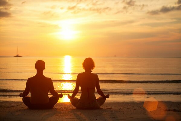 Homme et femme méditent au coucher du soleil au bord de la mer