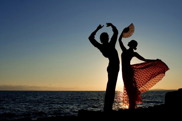 Silhouette of a guy and a girl in a dress with a fan standing in a dancing pose