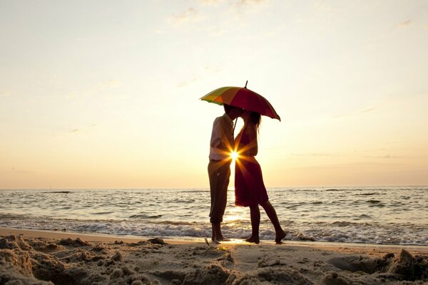 Liebhaber auf dem Hintergrund des Sonnenuntergangs am Meer mit einem Regenschirm in den Händen