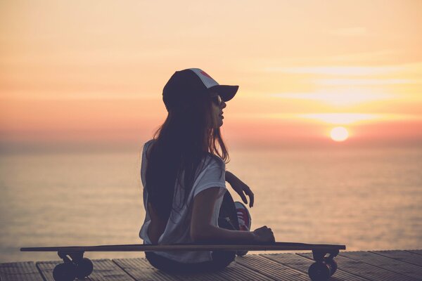 Mädchen in einer Kappe am Meer bei Sonnenuntergang