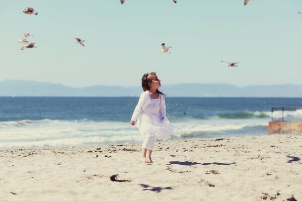 Chica en blanco en la playa con gaviotas