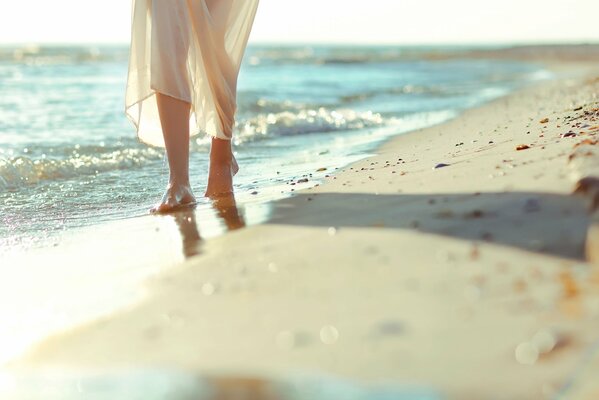 Piedi nudi che camminano sulla spiaggia ragazza in abito bianco